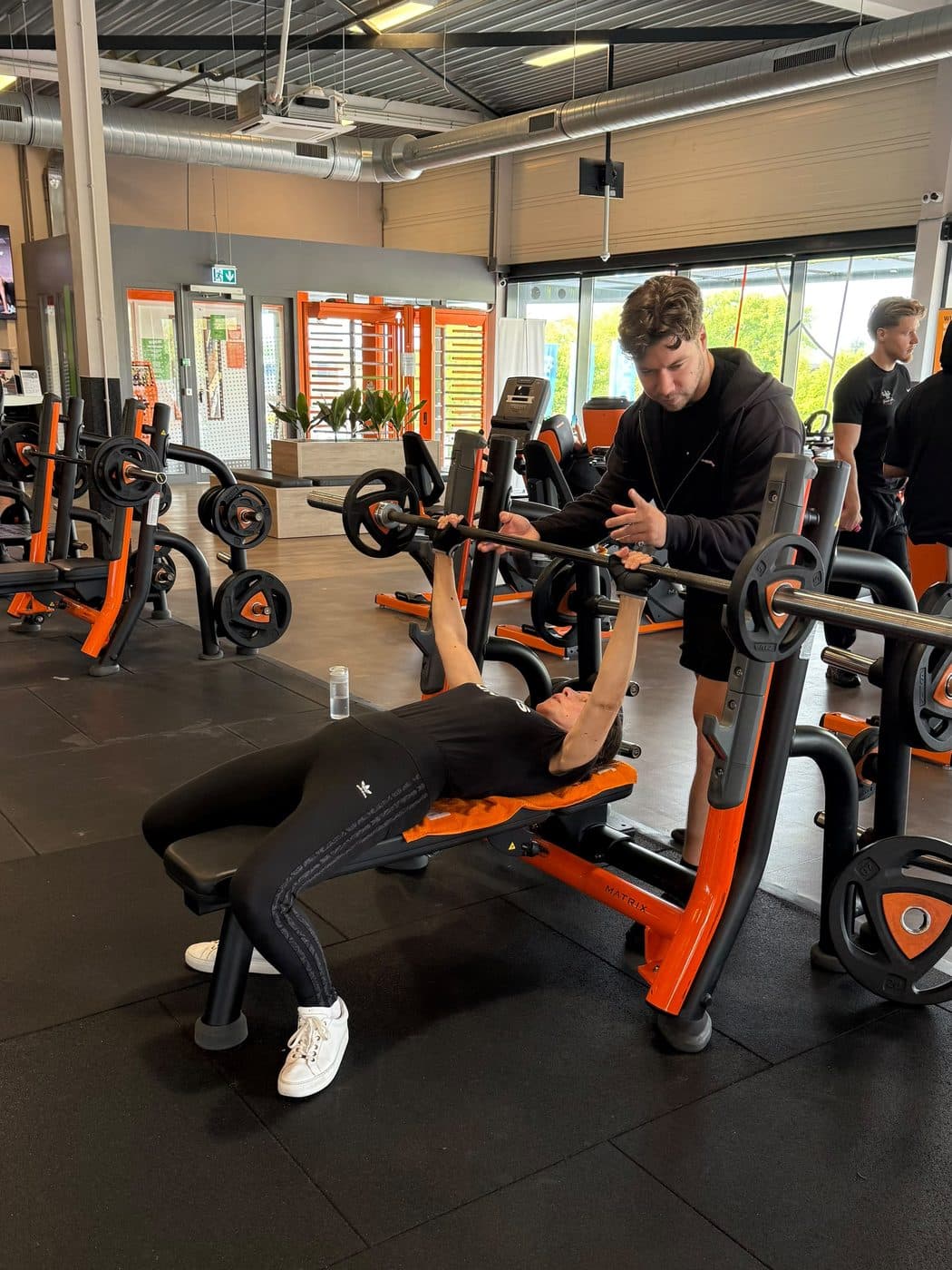 Rian begeleidt de stang terwijl een klant bankdrukt