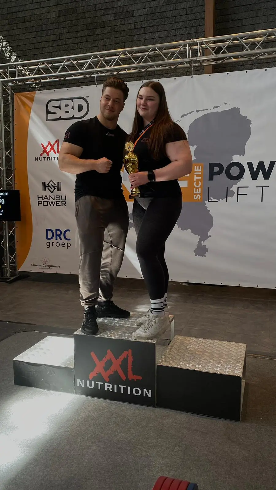Rian met een van zijn klantes op het podium van een powerliftingwedstrijd, met beker