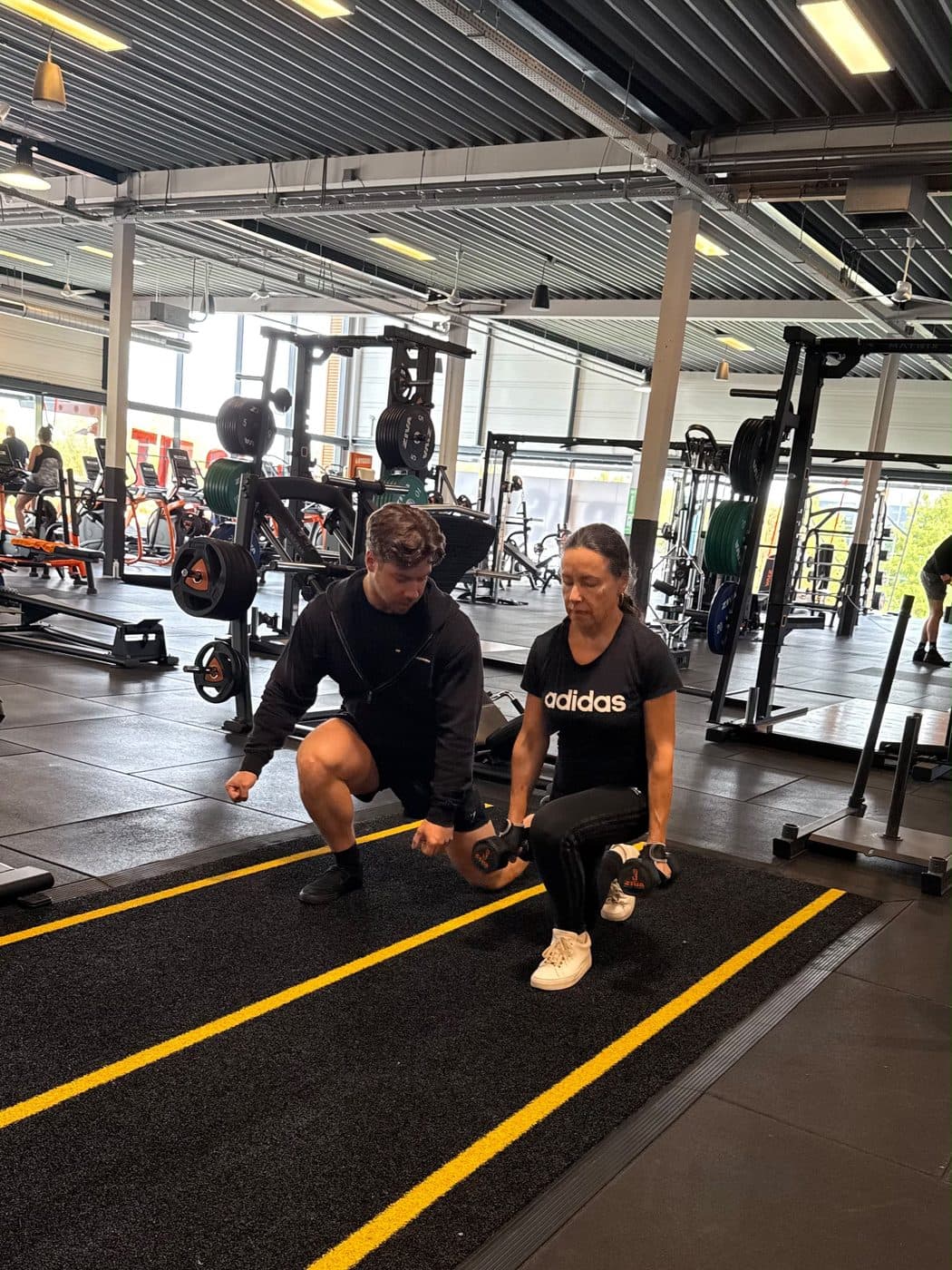 Rian hurkt naast een klant die lunges doet met dumbbells