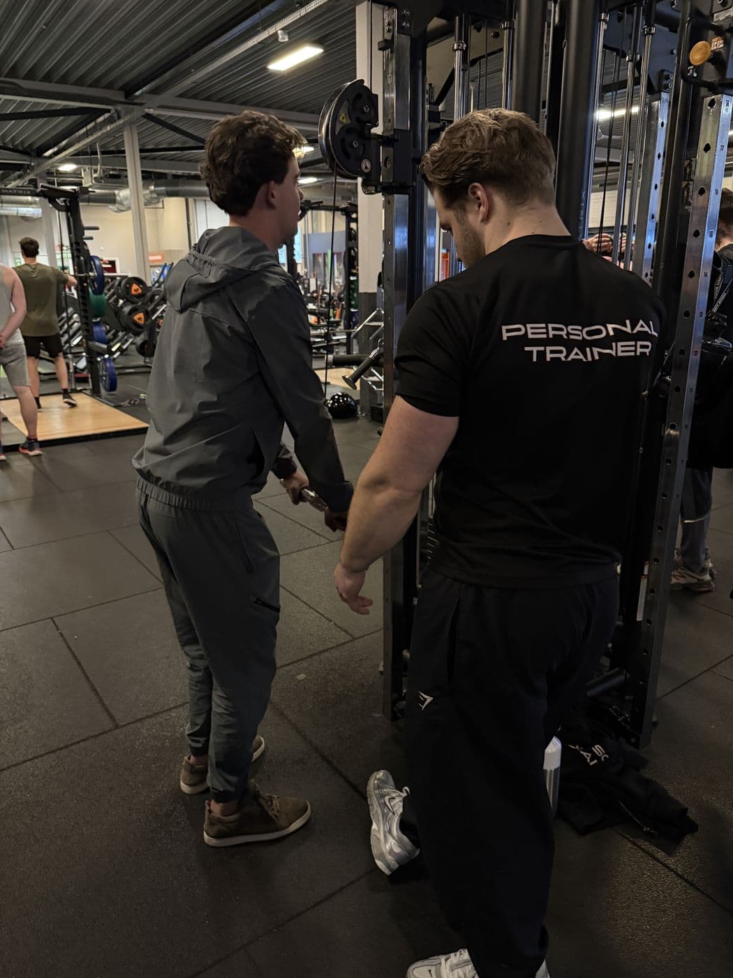 Rian begeleidt een klant bij een oefening aan de kabelmachine