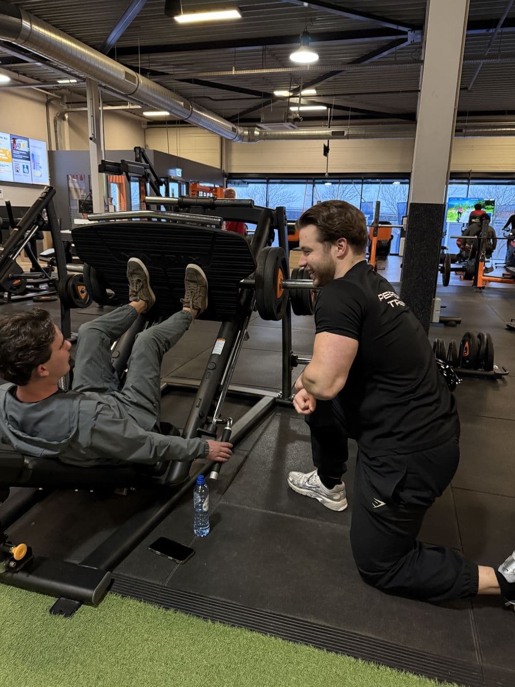 Rian kijkt mee terwijl een klant een set op de legpress afmaakt